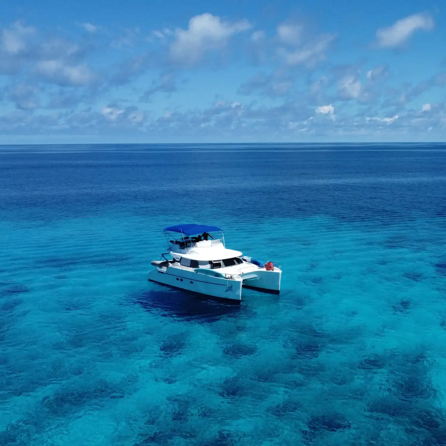 Luxury yacht sailing in clear blue ocean waters under a partly cloudy sky. Fontaine Pajot Maryland 37 power catamaran anchored at sea under clear skies